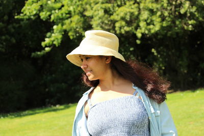 Portrait of south asian woman wearing hat standing against trees looking away