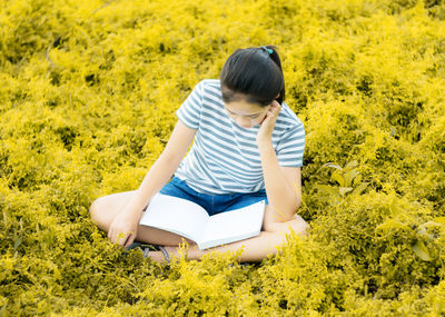 Full length of teenage girl reading book on field