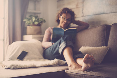 Young woman reading book while relaxing on sofa at home