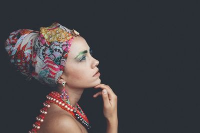 Side view of thoughtful woman wearing headscarf and necklaces looking away against black background