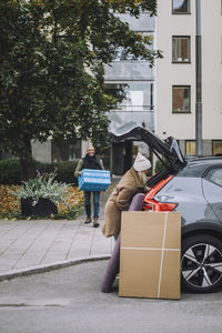 Couple helping each other while loading luggage in car trunk during relocation