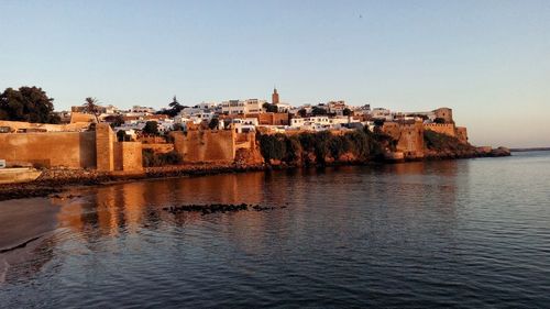 Buildings by sea against clear sky