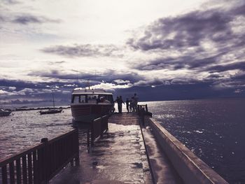 Rear view of people on pier at sea against sky