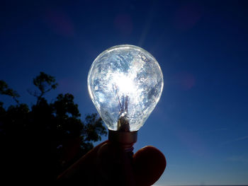 Close-up of hand holding crystal ball against trees at night