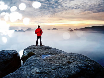 Rear view of man standing on rock against sea during sunset