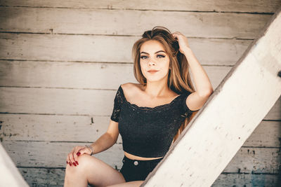 Portrait of young woman sitting against wall