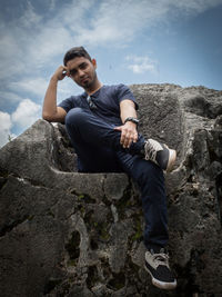 Portrait of young man on rock against sky