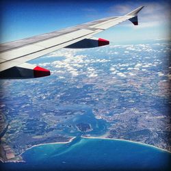 Cropped image of airplane flying over landscape against blue sky