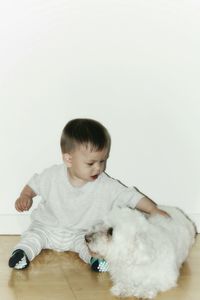 Toddler sitting with dog on floor against white wall