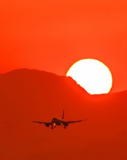 Low angle view of airplane flying against orange sky