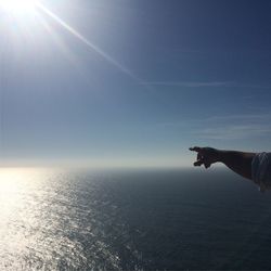 Close-up of hand by sea against sky