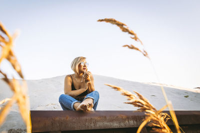 Young woman looking away while sitting against sky