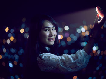 Close-up portrait of smiling young woman holding illuminated lighting equipment