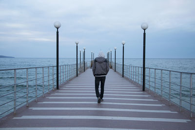 Rear view of man walking on pier over sea against sky