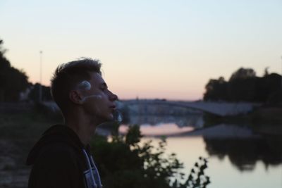 Portrait of young man looking away against sky during sunset