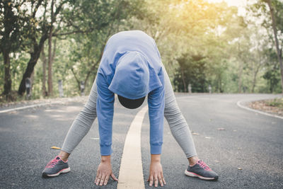 Woman exercising on road amidst trees