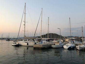 Sailboats moored in harbor at sunset