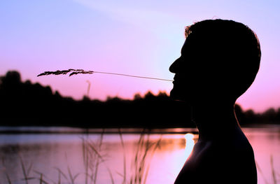 Silhouette man carrying grass in mouth by lake during sunset