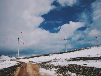 Low angle view of wind turbines on field against sky during winter