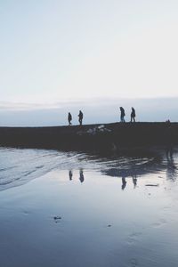 People walking on promenade by sea against sky