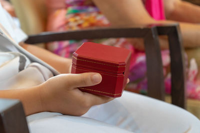 Midsection of boy holding jewelry box while sitting on chair