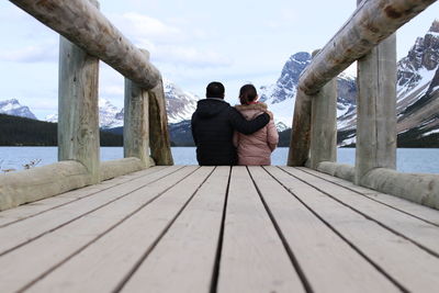 Rear view of people sitting on pier against sky