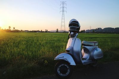 Motor scooter with helmet on road by grassy field against sky