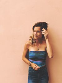 Young woman looking away while standing against wall