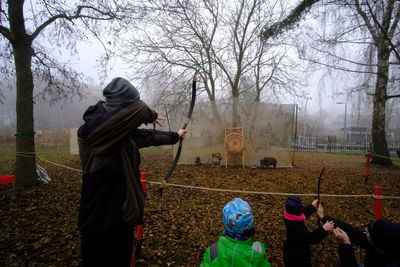 Rear view of woman photographing by trees