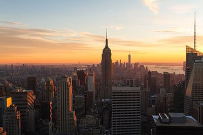 Empire state building amidst cityscape against sky during sunset