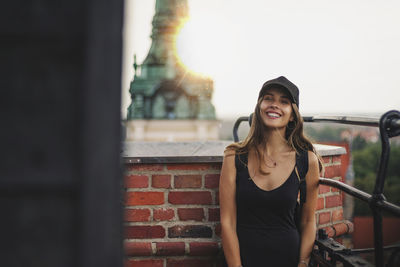 Portrait of smiling young woman standing against brick wall