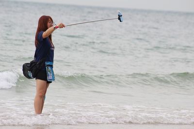 Side view of woman talking selfie while standing on shore at beach