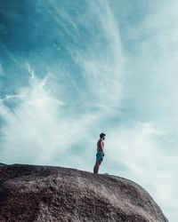 Low angle view of man standing on rock against sky