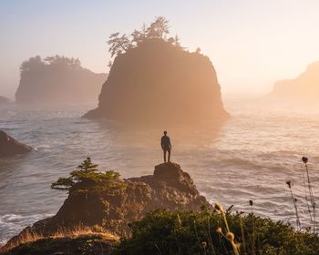 Silhouette man standing on cliff by sea against clear sky