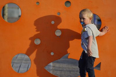 Cute boy looking away while standing by orange wall