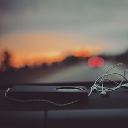 Close-up of mobile phone with in-ear headphones on car dashboard