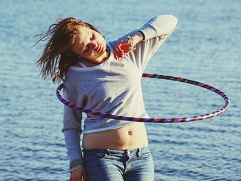 Young woman playing with plastic hoop against sea