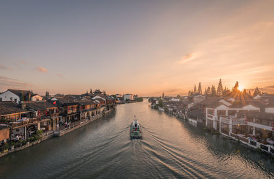 High angle view of boat sailing in river amidst buildings against sky during sunset