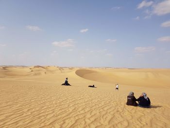 People on sand dune in desert against sky