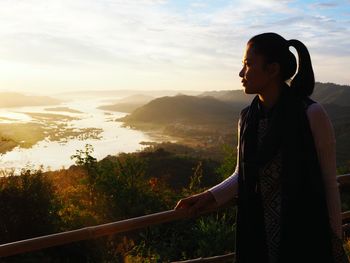 Woman looking away standing by railing against sky