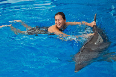 Happy beautiful young girl laughs and swims with dolphins in blue swimming pool on sunny day