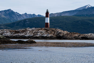 Lighthouse by sea and buildings against sky