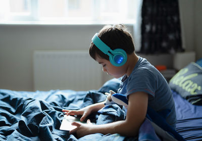 Side view of man using mobile phone while sitting on bed at home