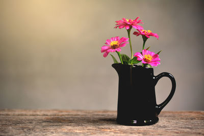 Pink flowers in pitcher on wooden table against wall