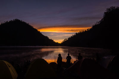 Silhouette people on lake against sky during sunset