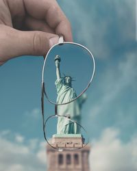 Cropped hand holding eyeglasses against statue of liberty