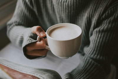 Midsection of person reading newspaper while holding coffee cup on table