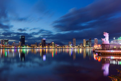 Illuminated city by river against sky at night