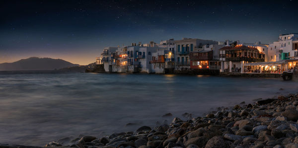 Illuminated houses by sea against sky at night