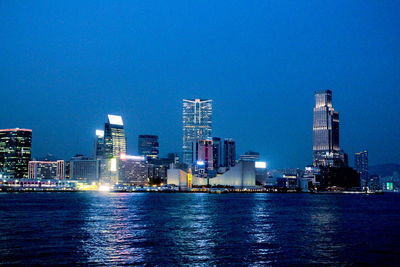 Illuminated buildings in city against clear blue sky